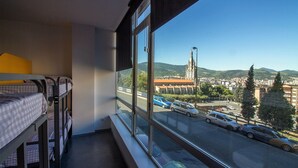 A room with bunk beds and a large window overlooking a cityscape with buildings and a hill. - All Iron Hostel (Bilbao)