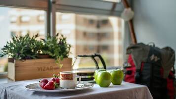 A table with a cup, strawberries, and green apples, a wooden box labeled 'VIZAR', and a window with a view of buildings.