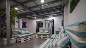 A modern lounge area with striped sofas and chairs, a potted plant, and a visible fire extinguisher. - All Iron Hostel (Bilbao)