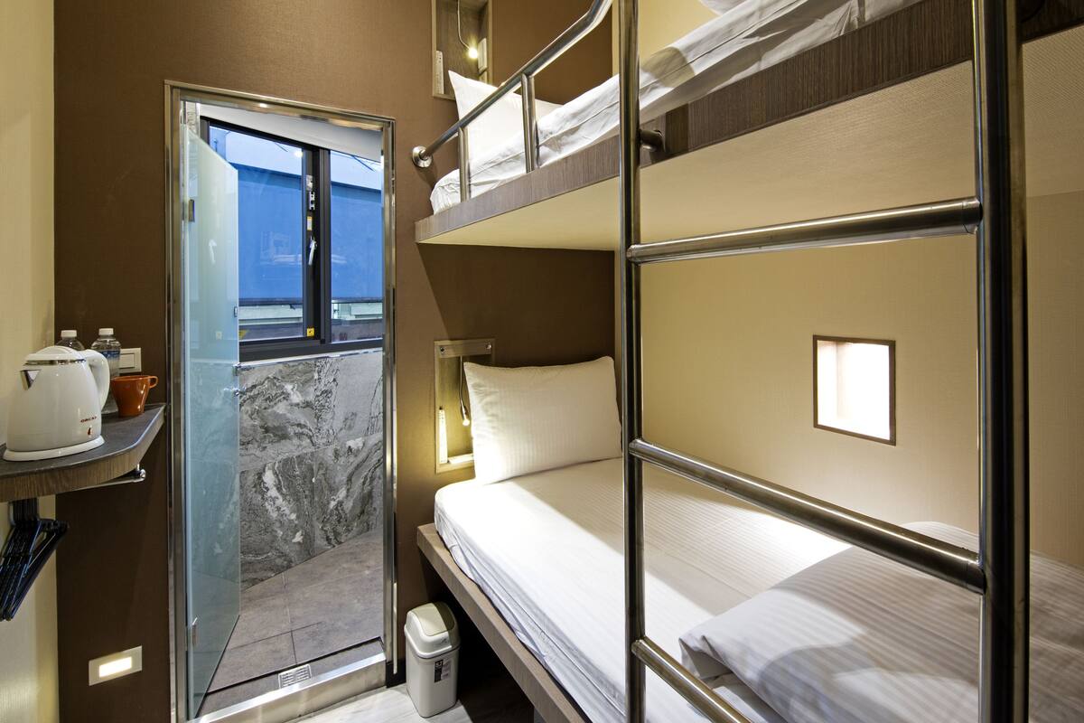 Habitación de hotel pequeña con literas, un kitchenette reducido y vistas a través de una puerta.