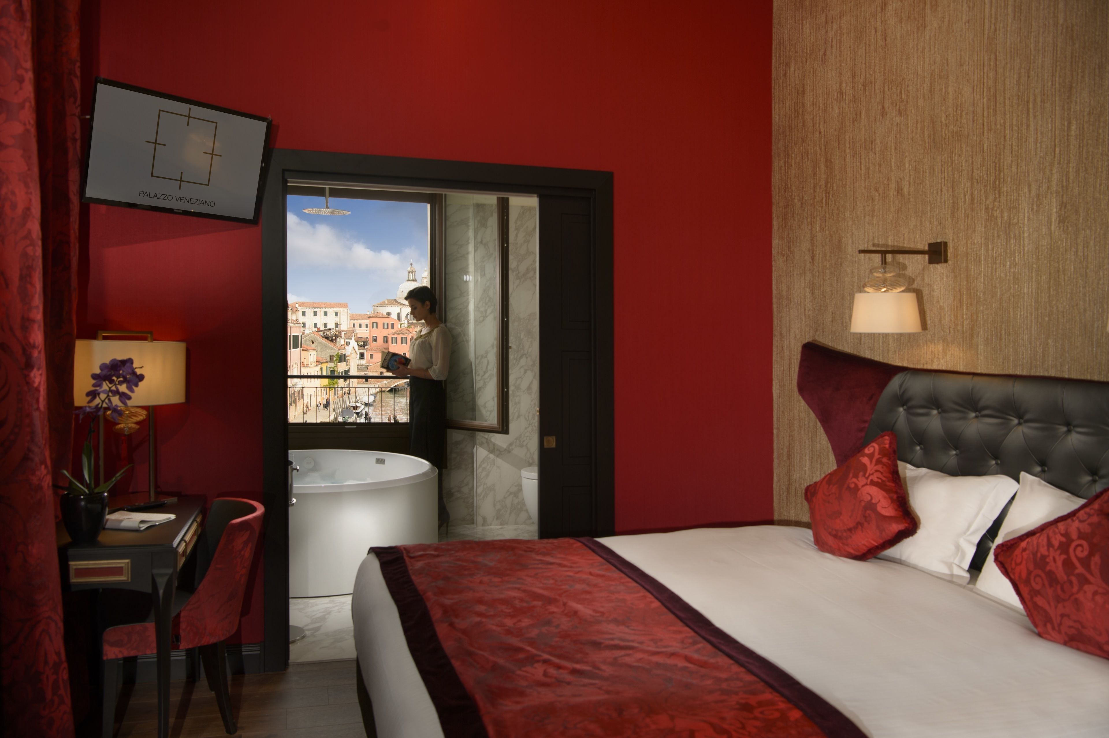 Een hotelkamer met een bed, een bureau met stoel, een raam met uitzicht op gebouwen en een badkamer met toilet en wastafel.