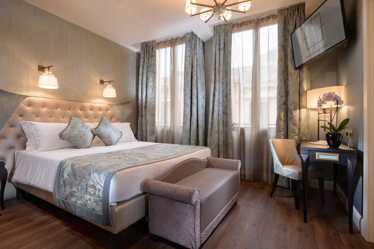 Ein Schlafzimmer mit einer gesteppten Kopfteil, einem Bett mit einem gemusterten Überwurf, einem Schreibtisch mit Stuhl und einem an der Wand montierten Fernseher.