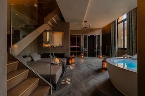 A modern interior with a curved bathtub, a wooden staircase, and a seating area with a fireplace. - Palazzo Veneziano (Venice)