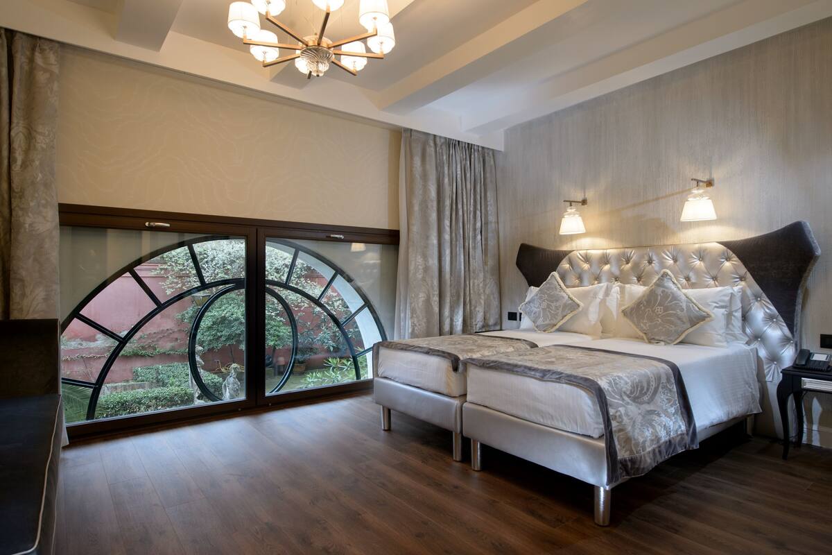 Ein Schlafzimmer mit einem großen Bett, zwei Nachttischen, einer Chandelüster und Blick durch ein großes Fenster.