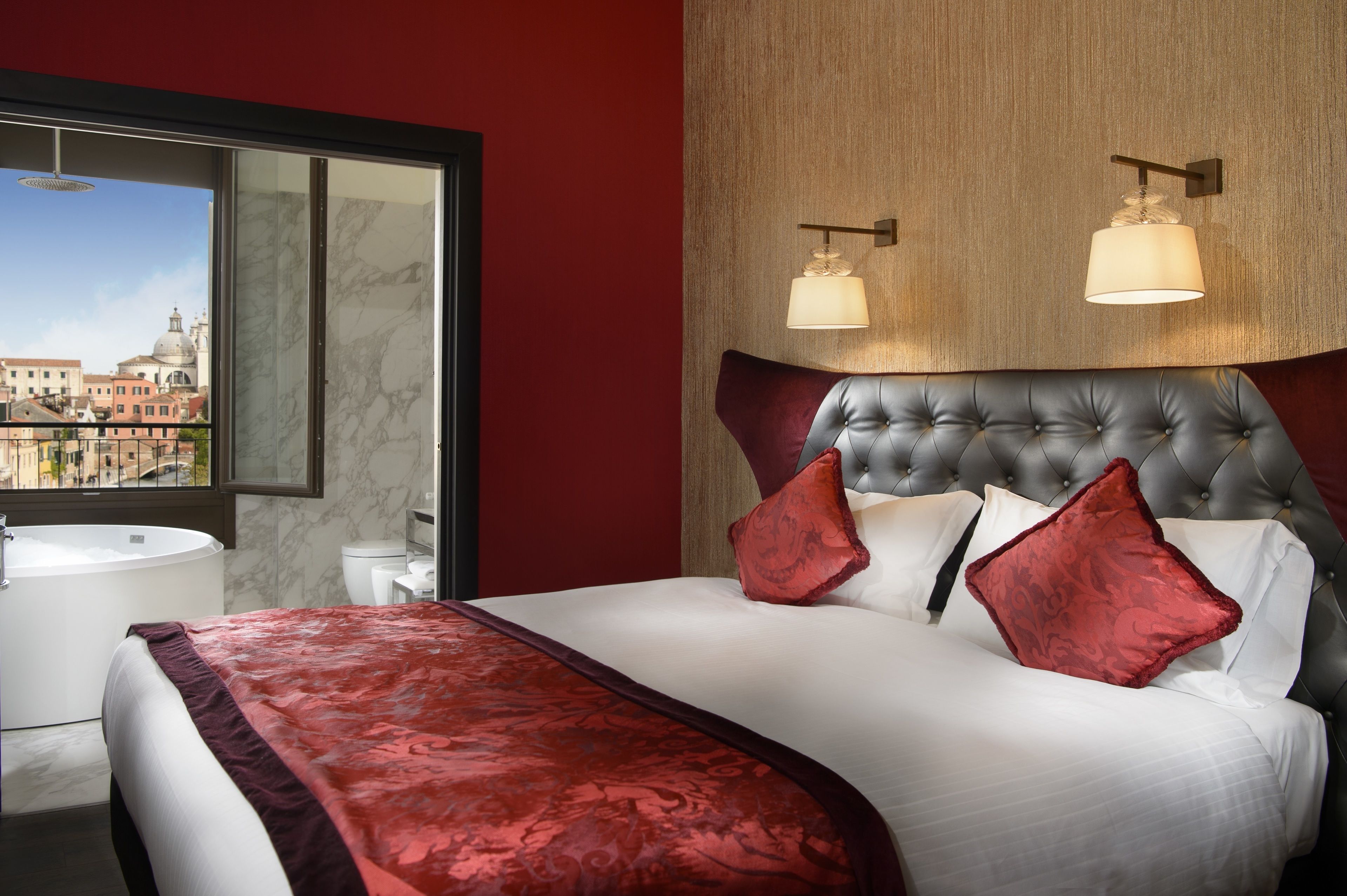 A hotel room with a large bed, a view of the city through a window, a round bathtub, and a modern bathroom.