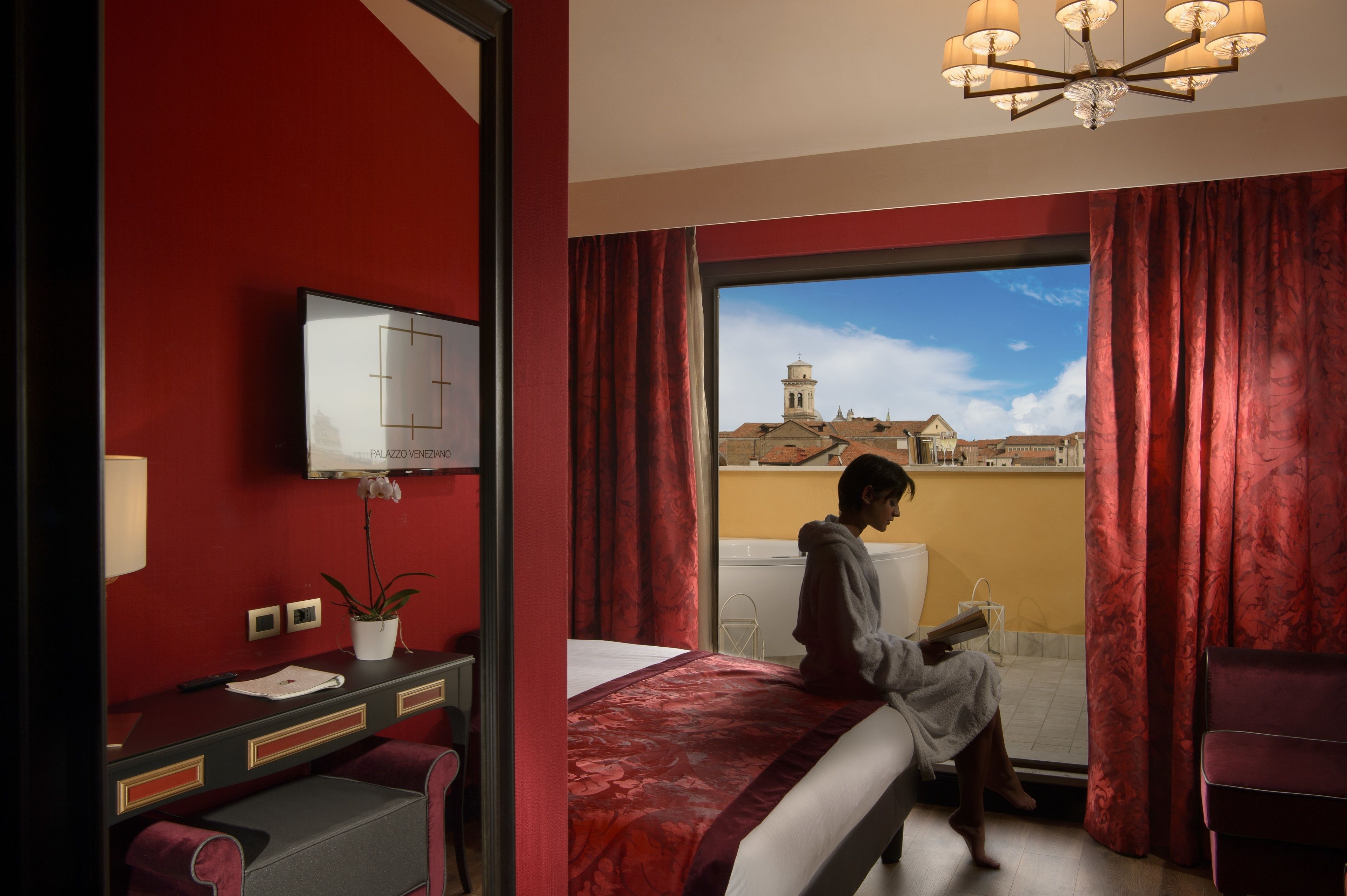 A hotel room with a bed, a desk, a chair, a TV, and a view of a building outside.