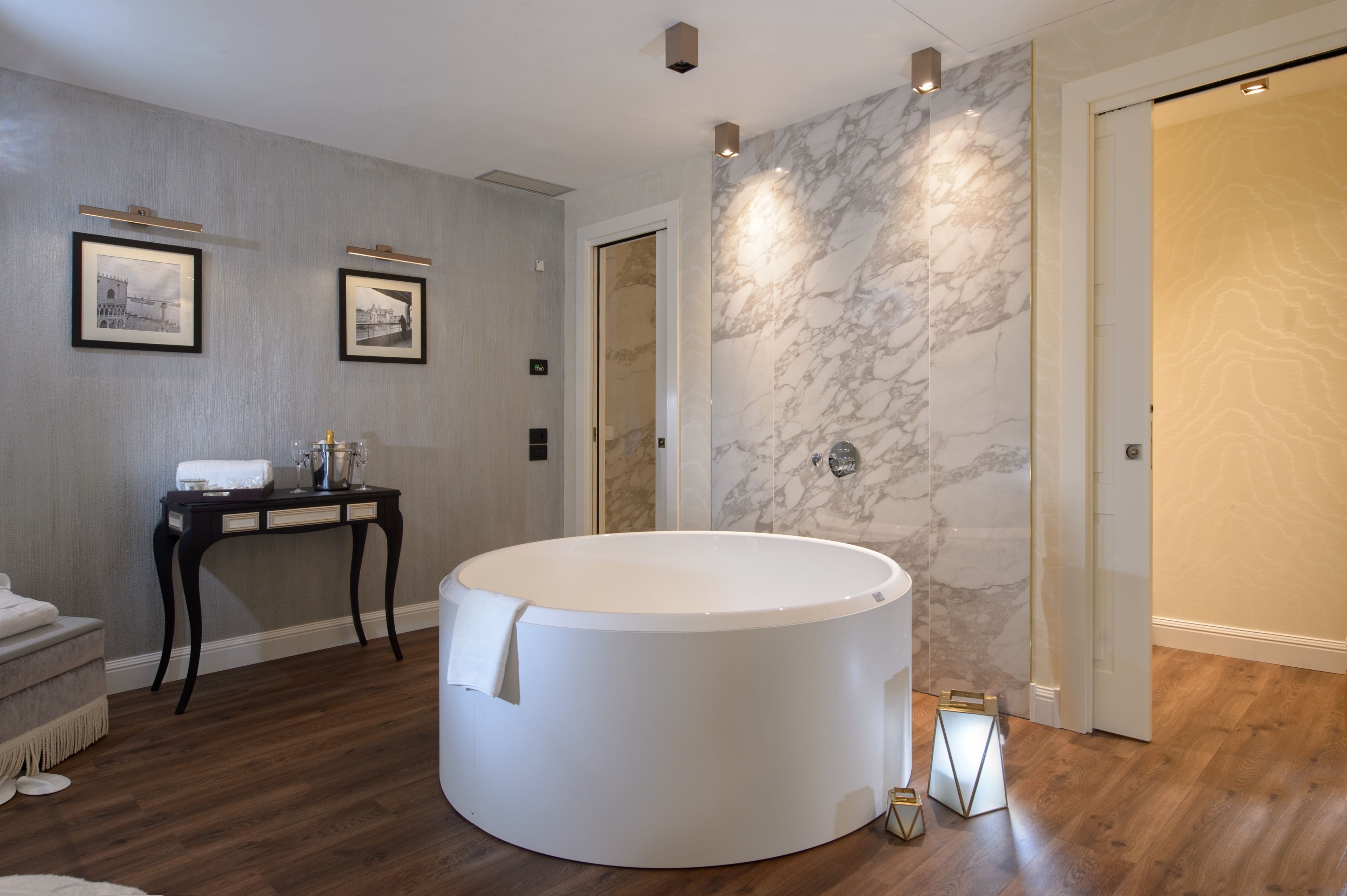 A modern bathroom with a large round bathtub, marble walls, and framed pictures on the wall.