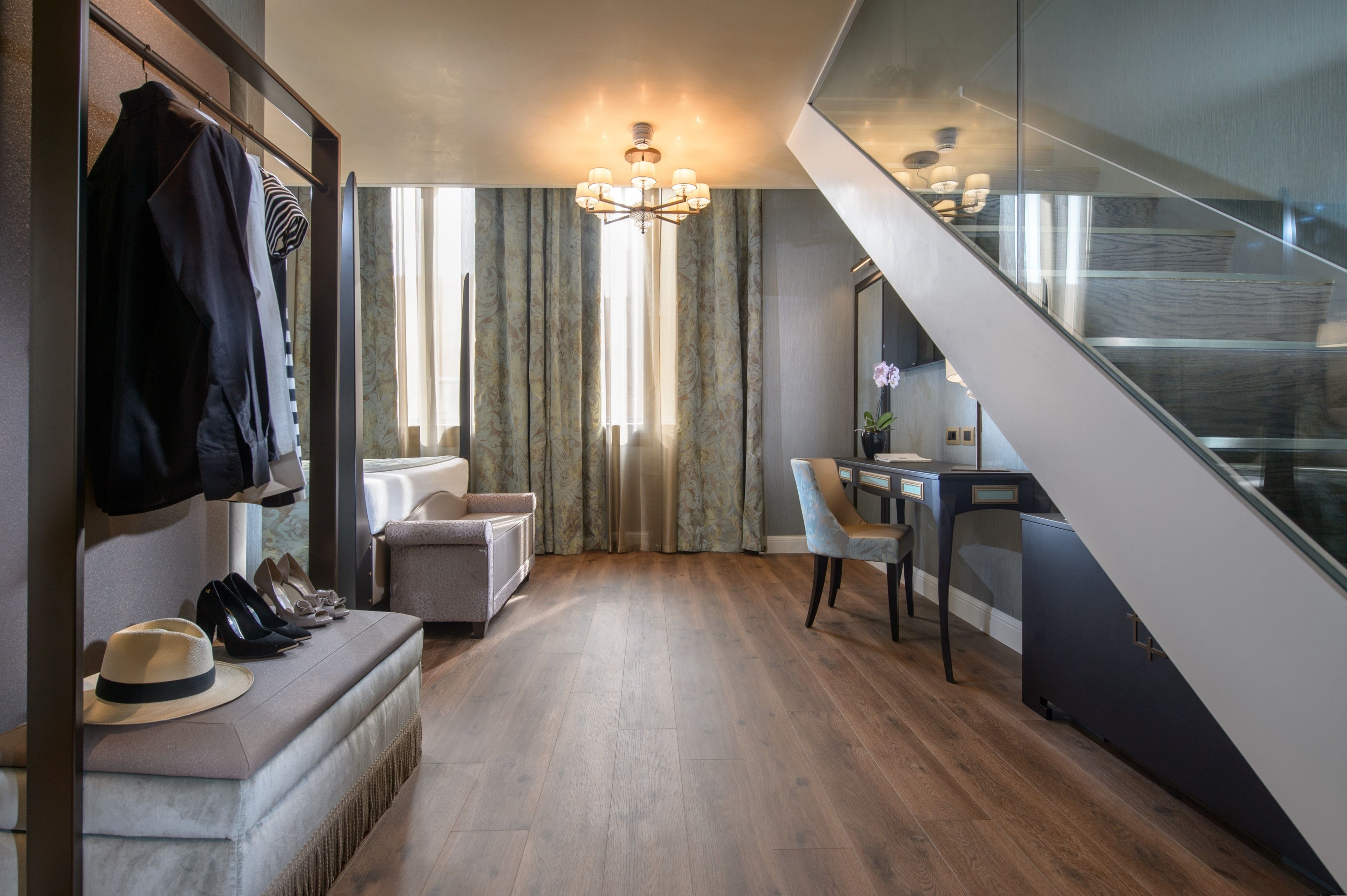 A modern hotel hallway with a staircase, a seating area with a bench, and a small table with chairs.