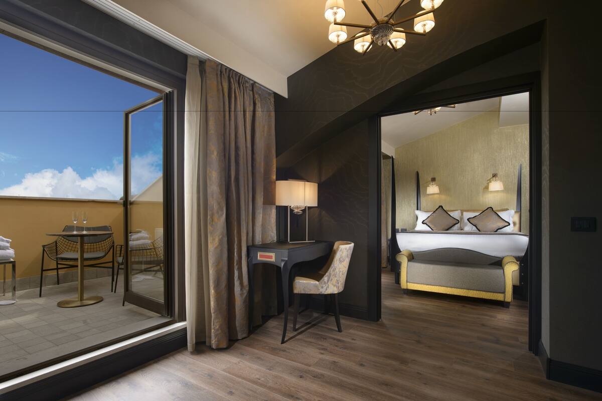 Ein Hotelzimmer mit großem Fenster, einem Schreibtisch mit Stuhl, einem Bett mit Kissen und einer Kandelaber.