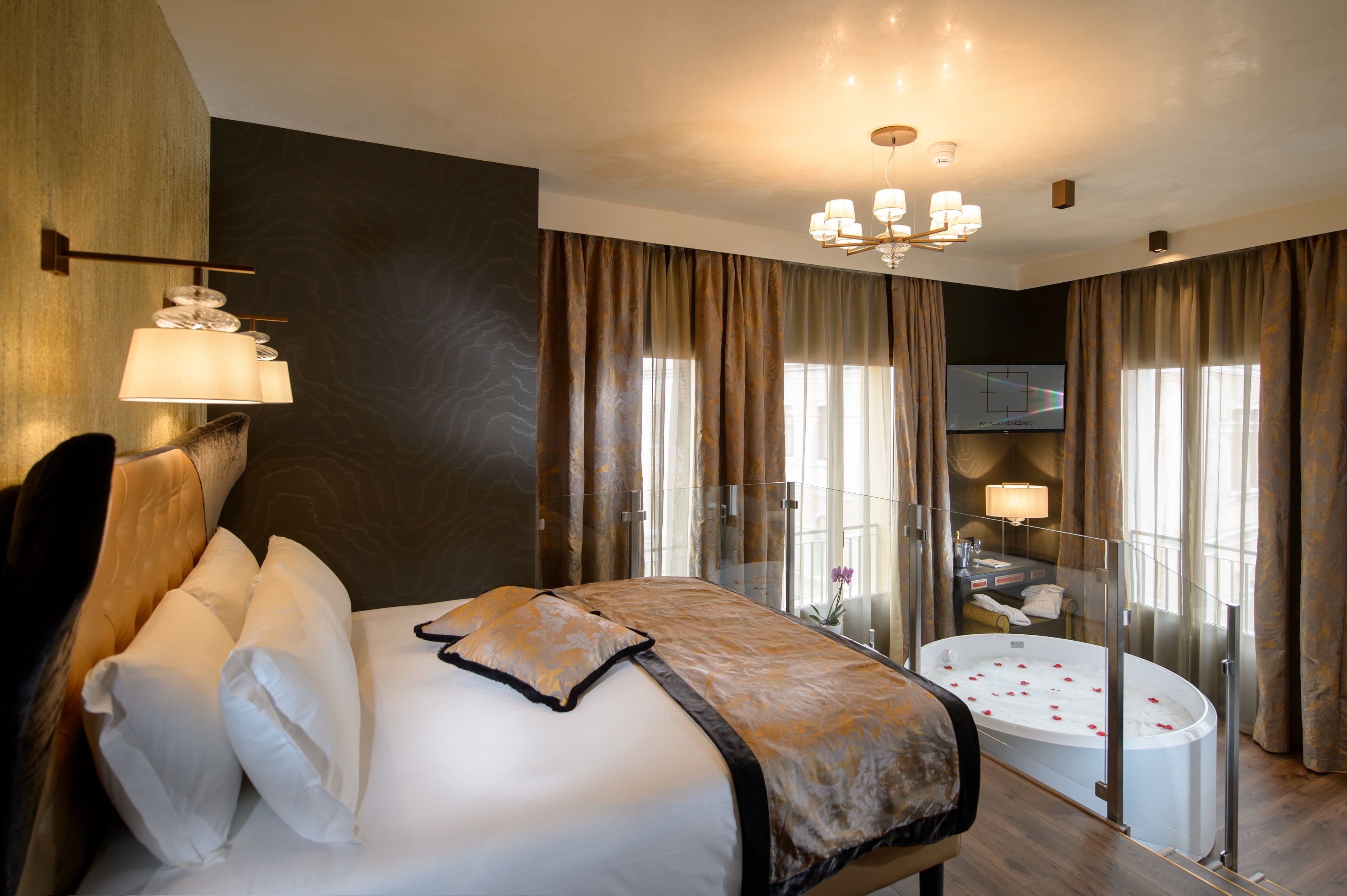 A hotel room with a large bed, a glass-enclosed bathtub, and a view of the city.