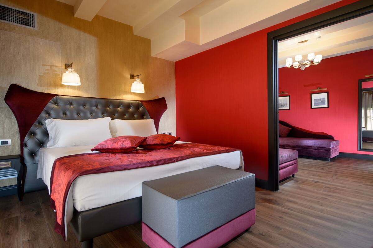 Ein modernes Schlafzimmer mit einer gesteppten Kopfteil, einem großen Bett mit rot-weißer Bettwäsche, einer grauen Bank und einer roten Akzentwand.