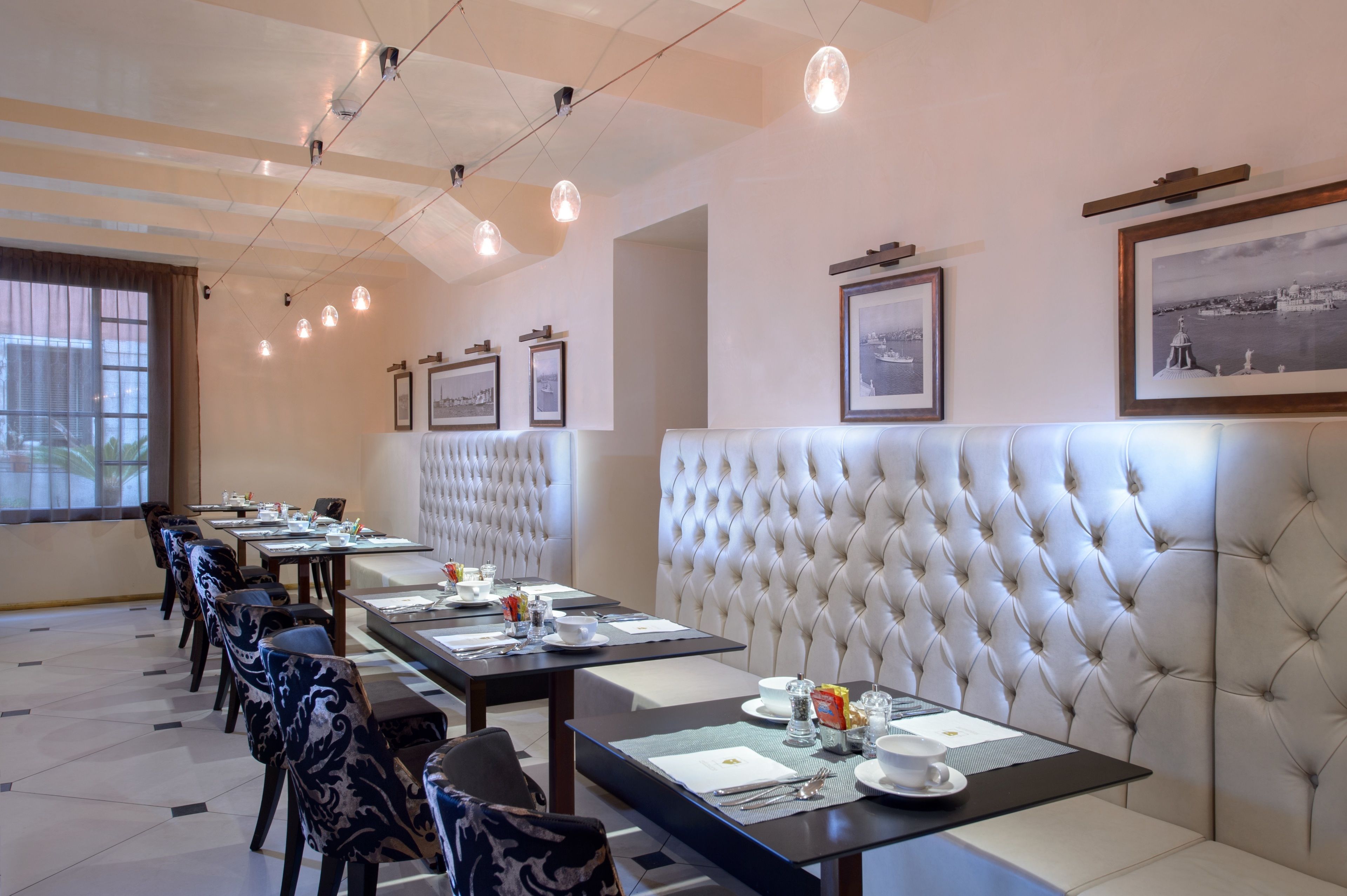 Un comedor con mesas largas, asientos acolchados e imágenes enmarcadas en las paredes.