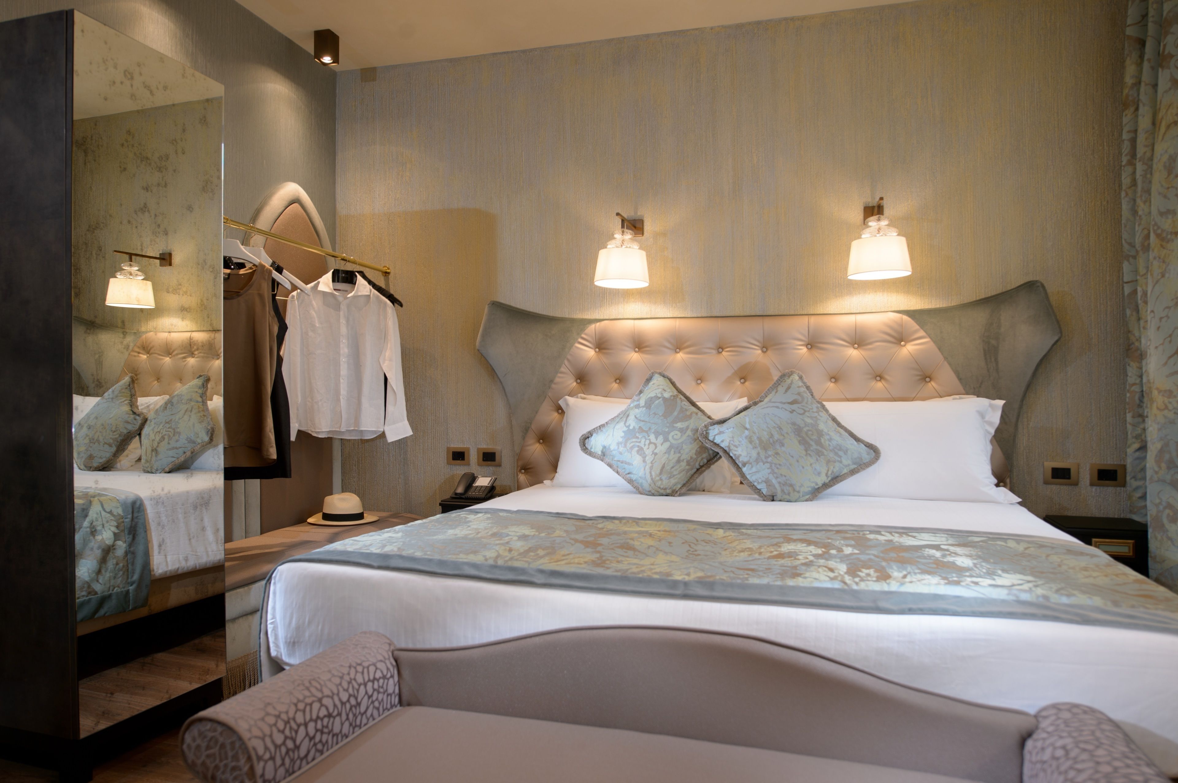 A bedroom with a large bed, a mirror, a wardrobe, and two wall-mounted lights.