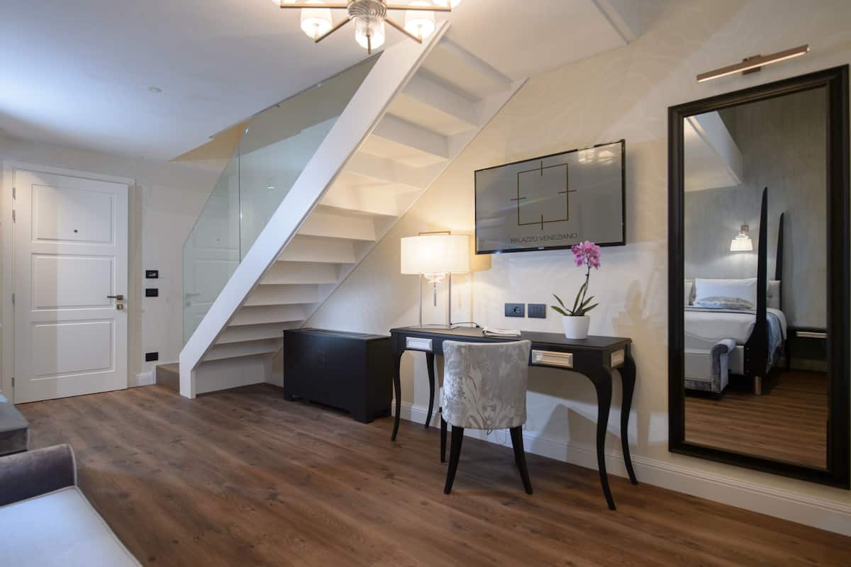 Ein modernes Zimmer mit Holzboden, Schreibtisch mit Stuhl, großem Spiegel und einer Treppe.
