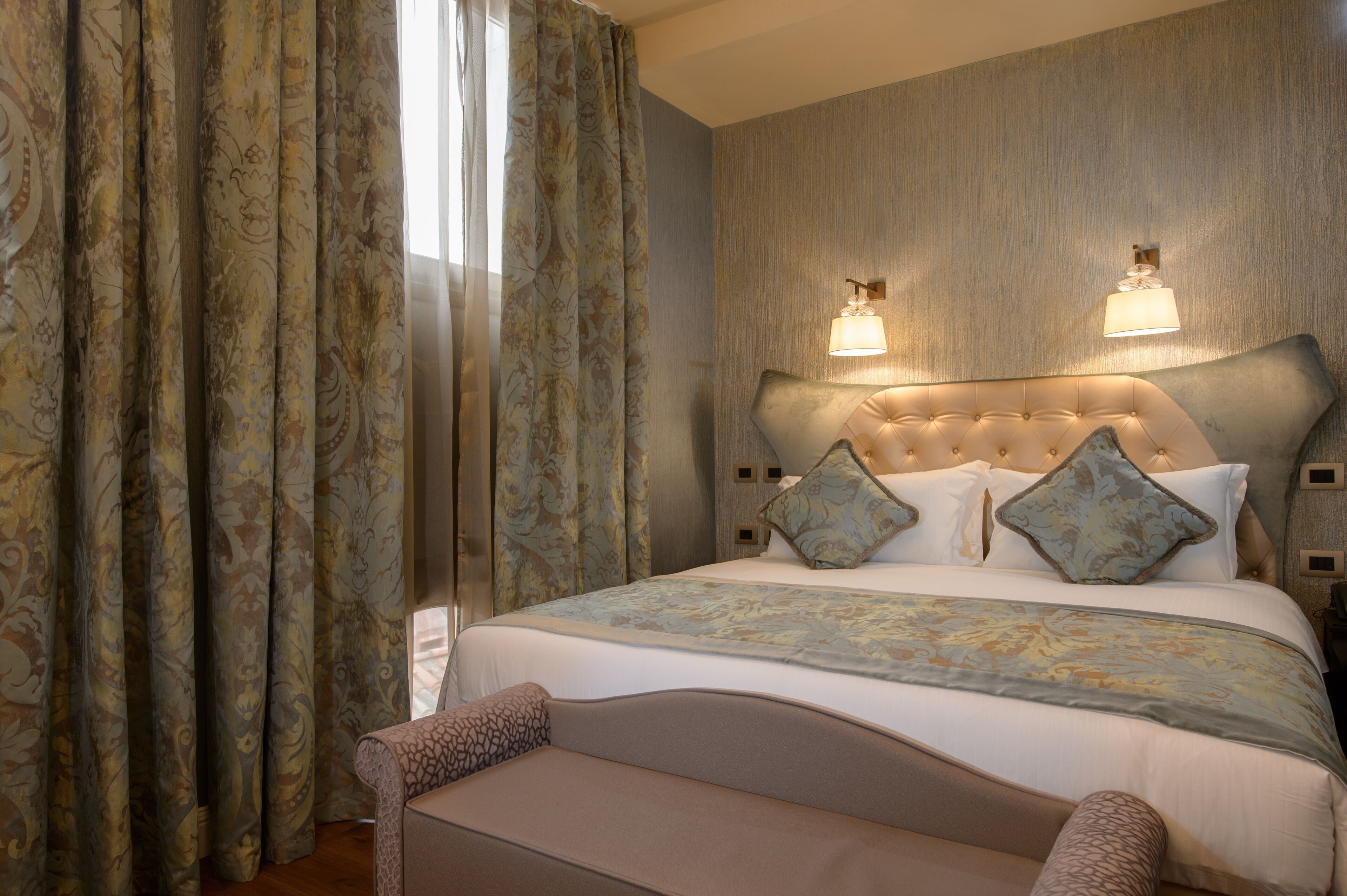 A hotel room with a large bed, two wall-mounted lamps, and a patterned curtain.