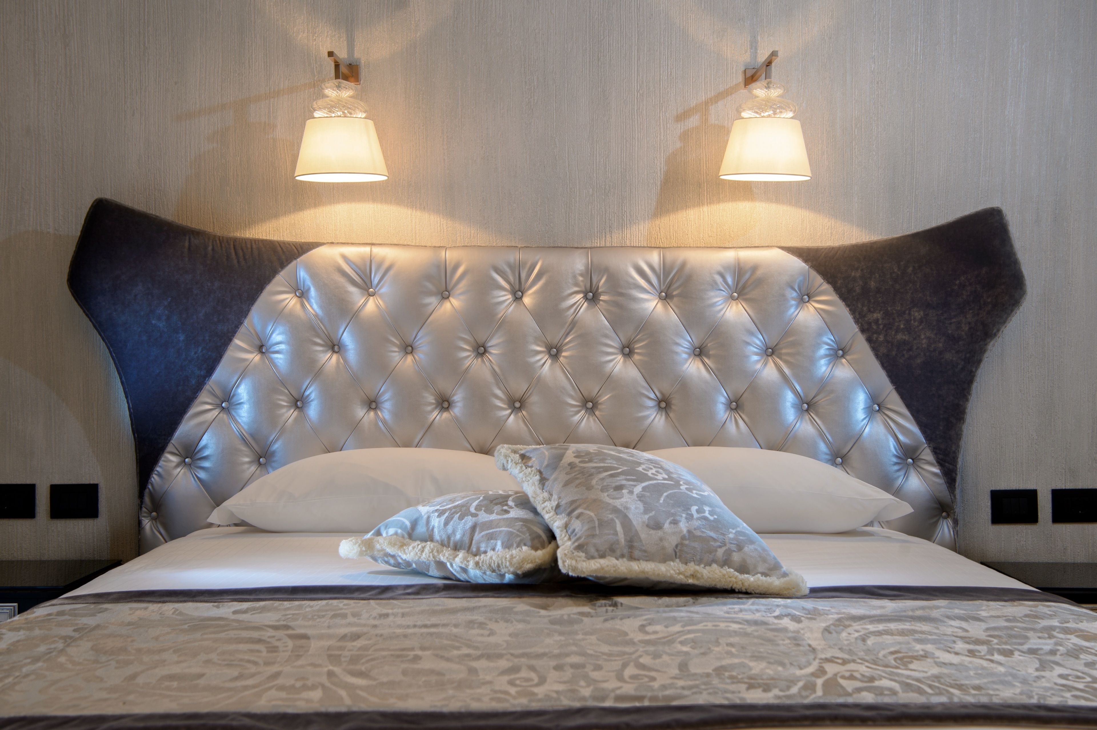 A bed with a tufted headboard, two wall-mounted lamps, and patterned bedding.
