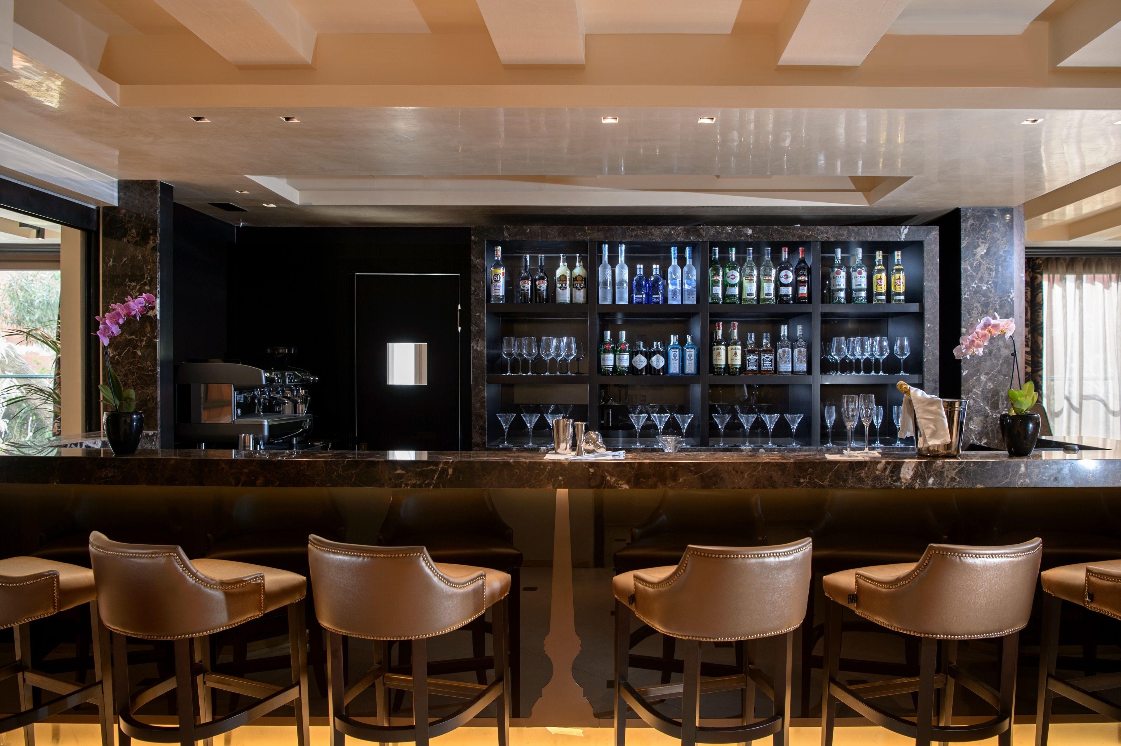 A bar area with a marble countertop, multiple liquor bottles, and bar stools.