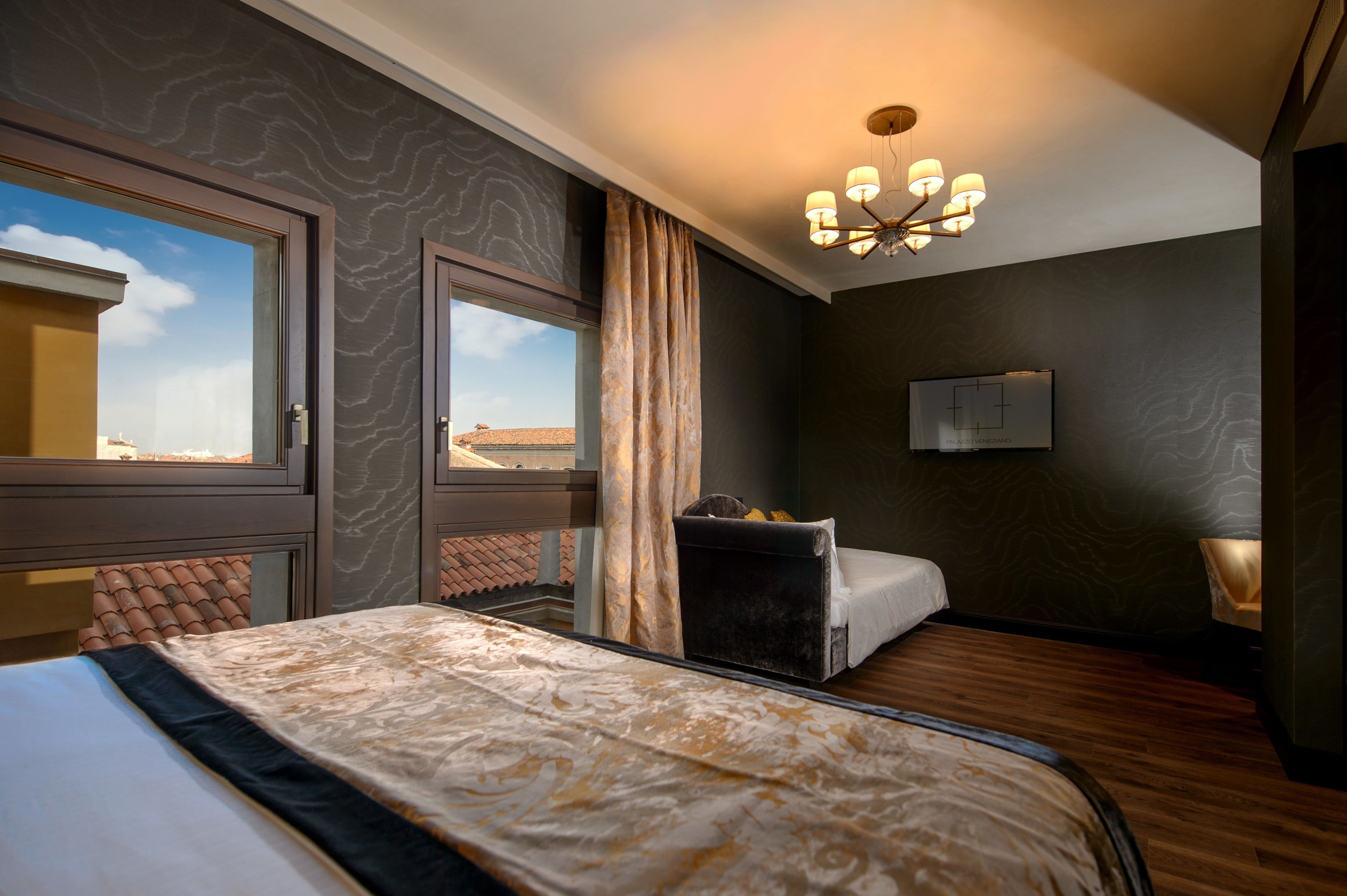 Une chambre d’hôtel avec un grand lit, une fenêtre donnant sur la ville, un lustre et une petite table avec une lampe.