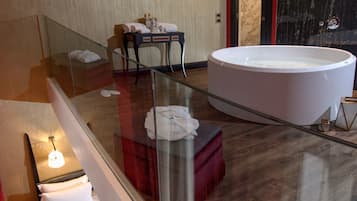Quarto de hotel moderno com varanda envidraçada, uma banheira grande e área de estar com mesa e cadeiras.