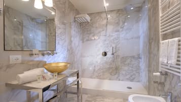A modern bathroom with a marble wall, a large mirror, a gold basin, a bathtub, and a shower area.