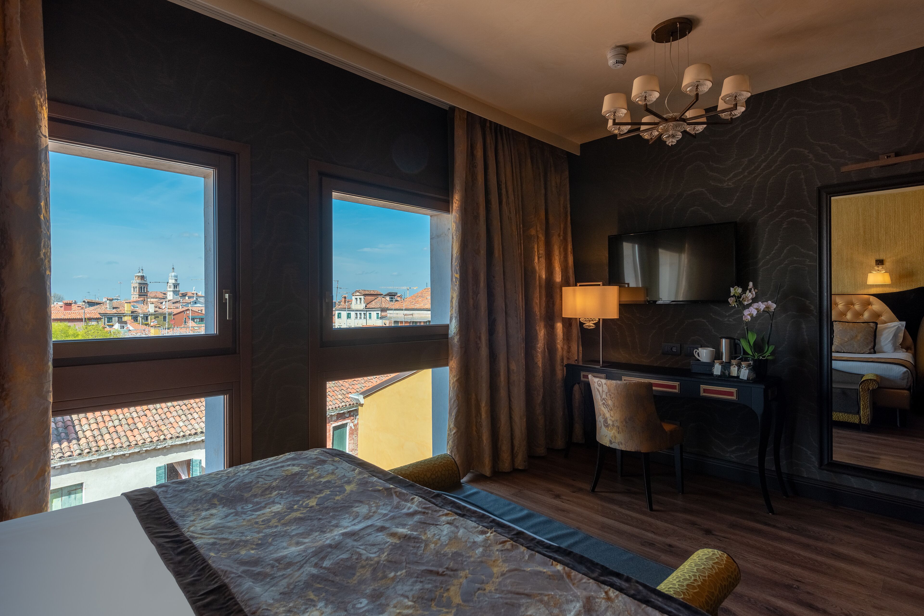 A hotel room with a large bed, a desk, a chair, a TV, and a view of the city.
