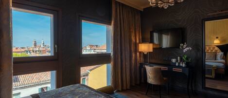 A hotel room with a large bed, a desk, a chair, a TV, and a view of the city.