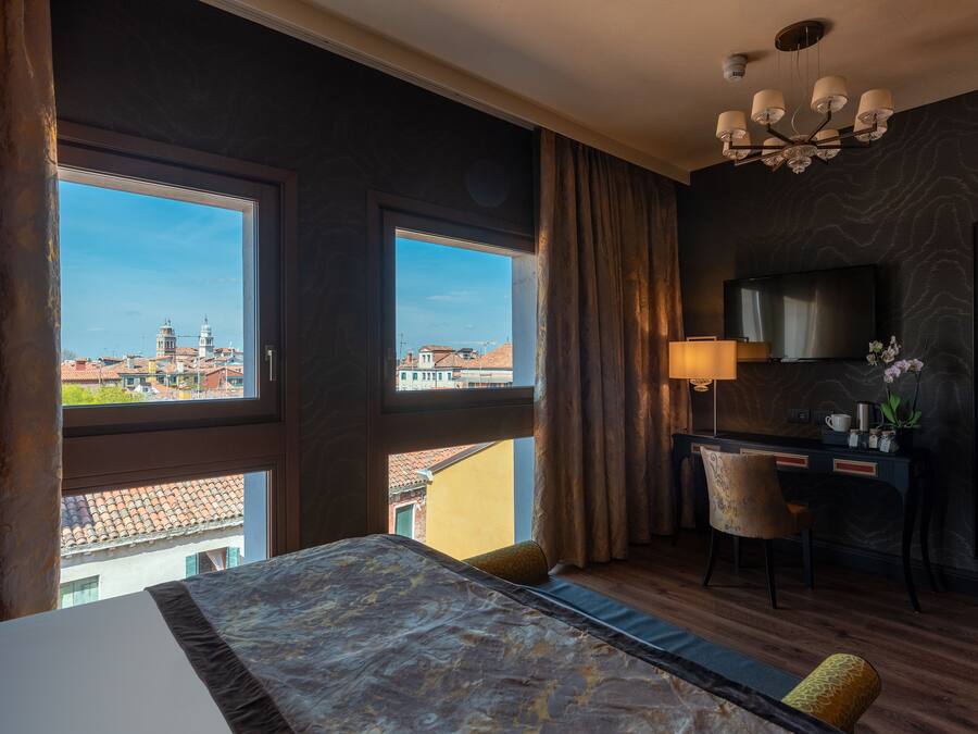Habitación de hotel con una cama grande, un escritorio, una silla, un televisor y vistas a la ciudad.