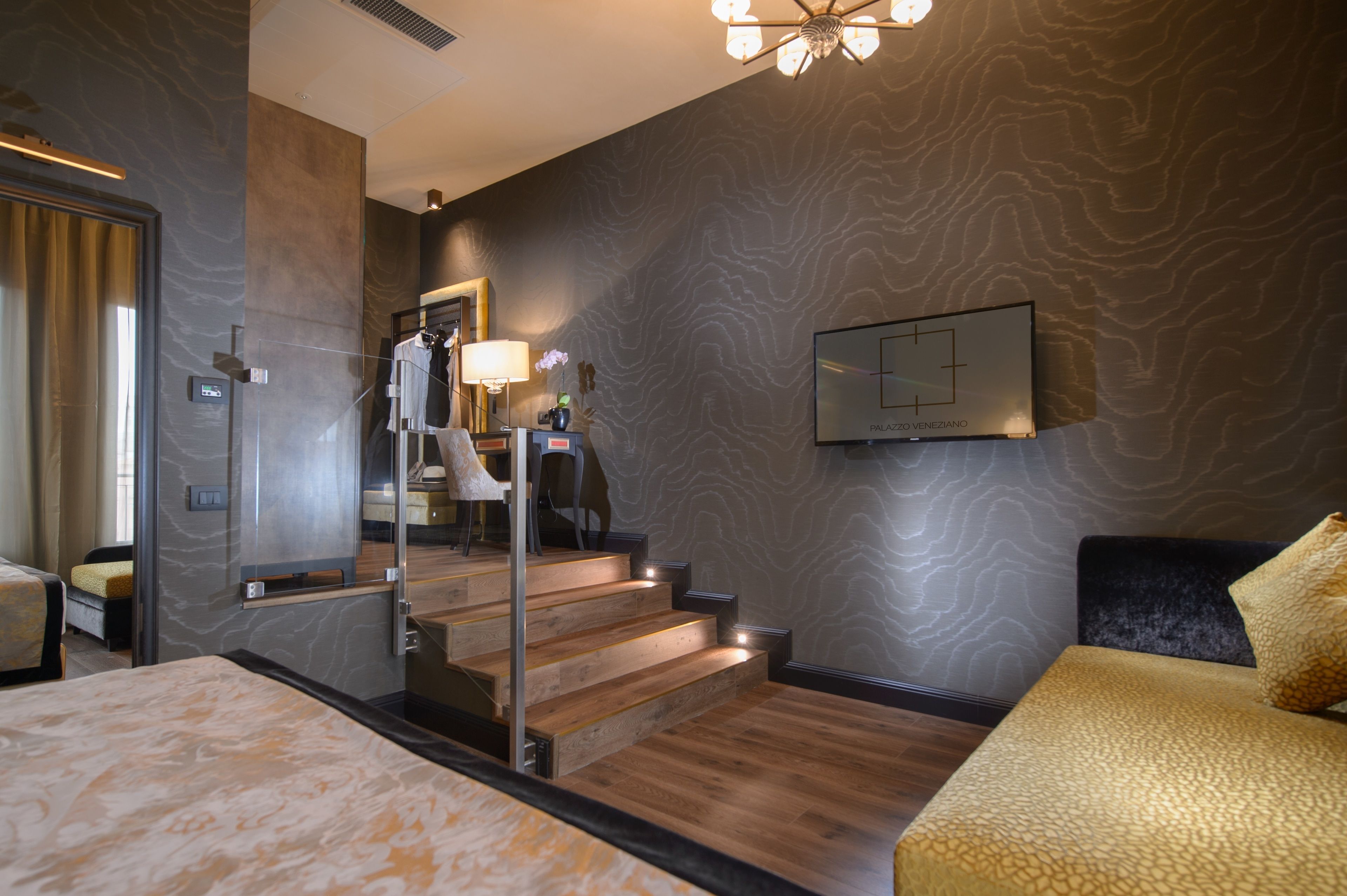 A modern hotel room with a large bed, a wooden staircase, a flat-screen TV, and a mirror.