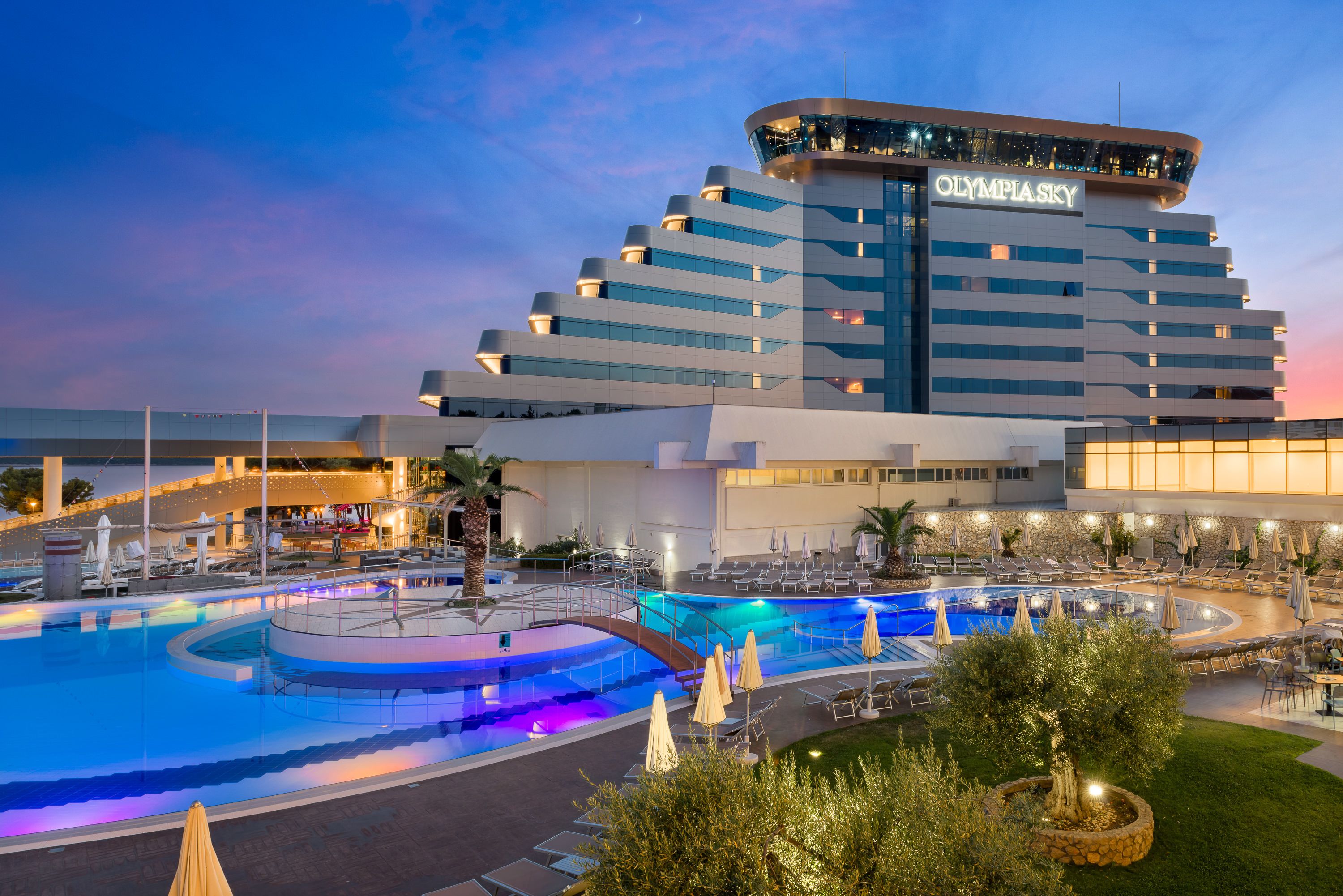 A hotel with a large swimming pool, outdoor seating, and a distinctive curved building.