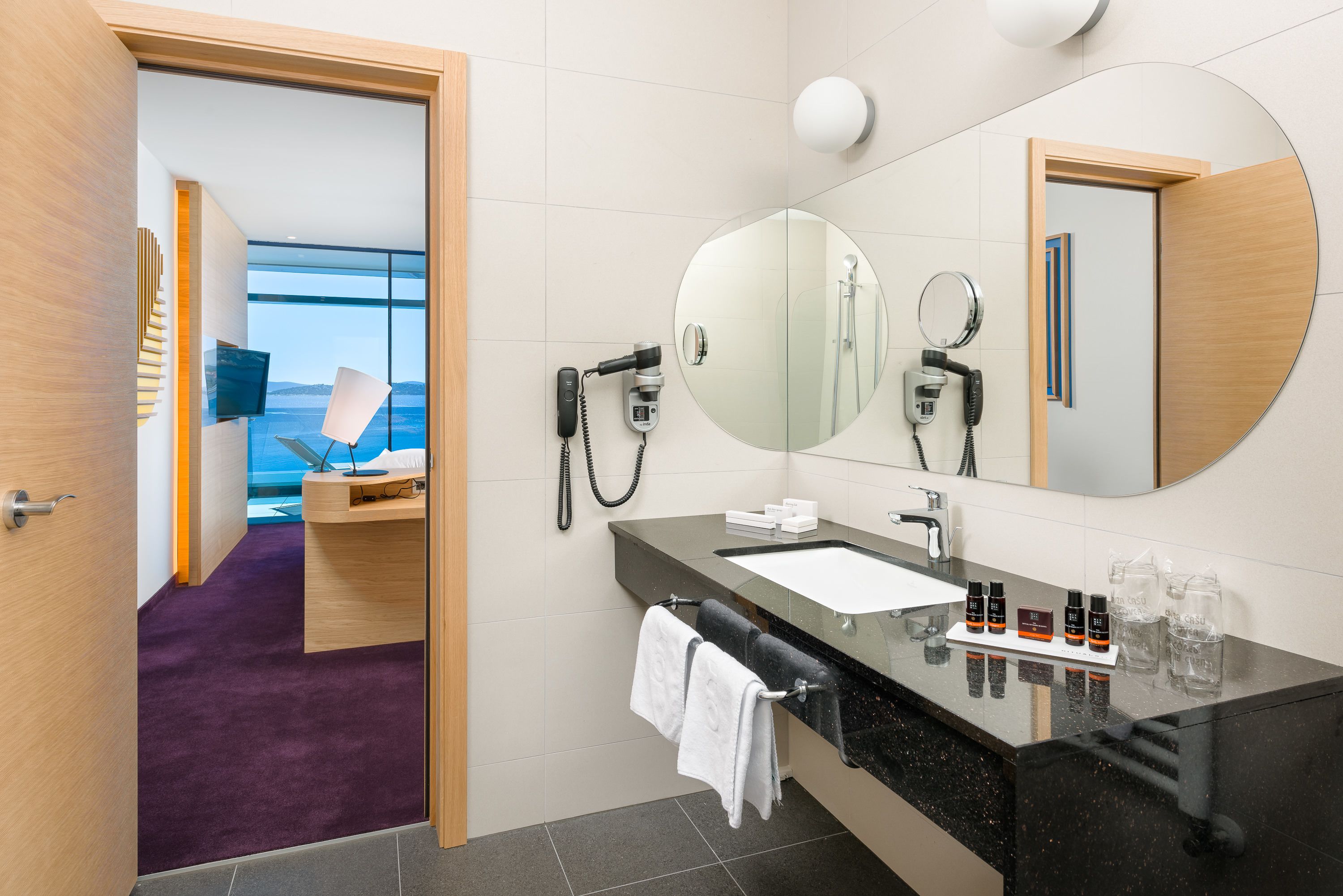 Een moderne badkamer met een grote spiegel, een wastafel en een haardroger.
