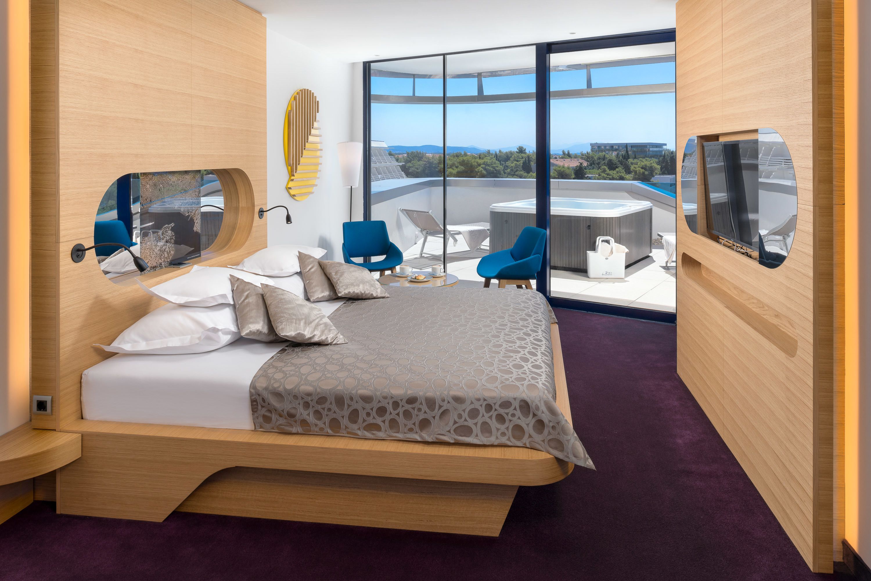 A modern hotel room with a large bed, a balcony with a hot tub, and a city view.