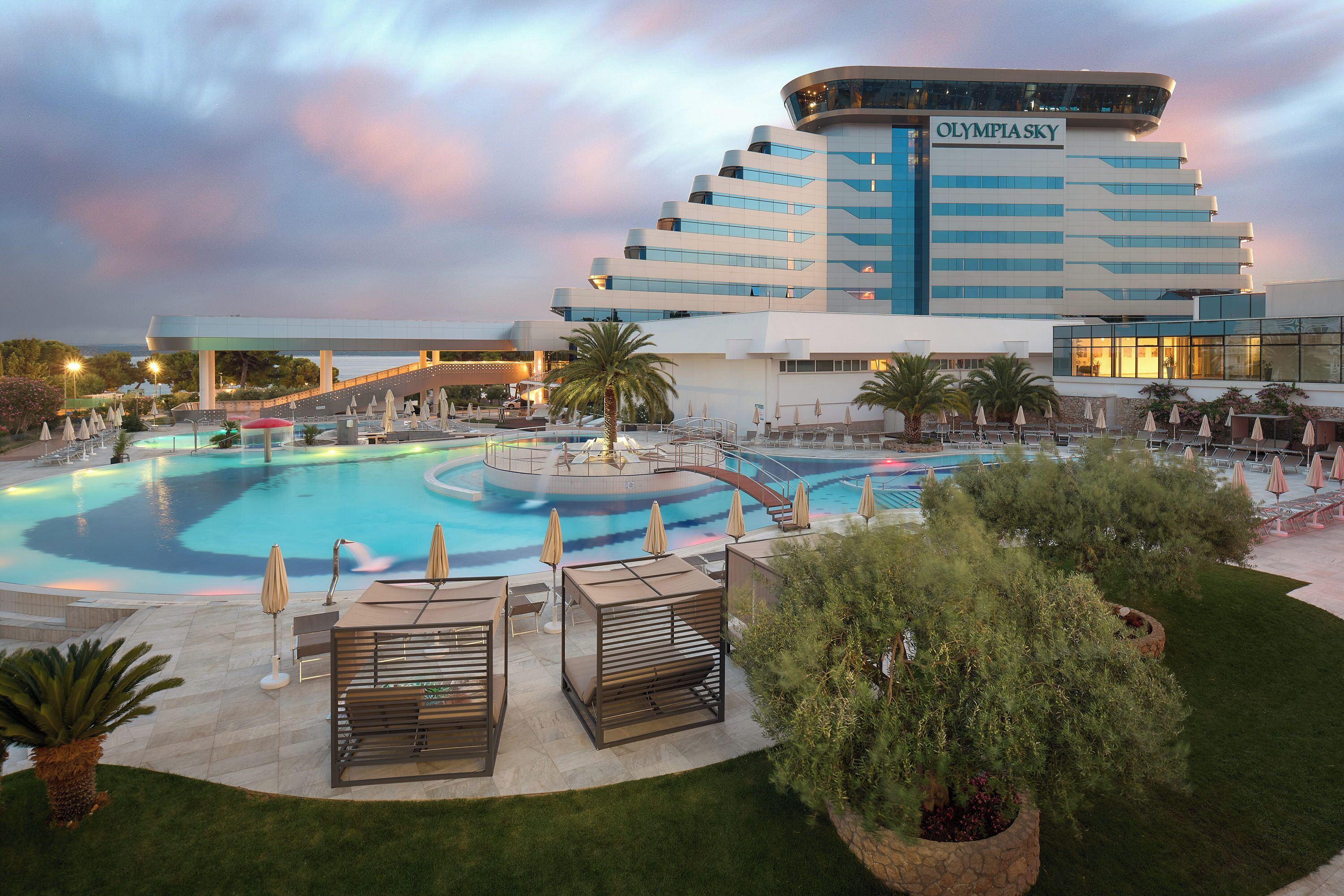 Um hotel com uma piscina grande, área de estar externa e um edifício moderno com o nome "Olympia Sky".