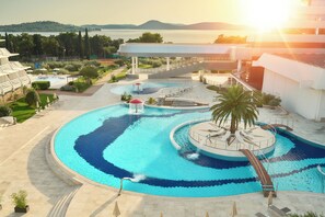 A resort pool with a circular design, a palm tree, and a view of the sea. - Hotel Olympia Sky (Vodice)