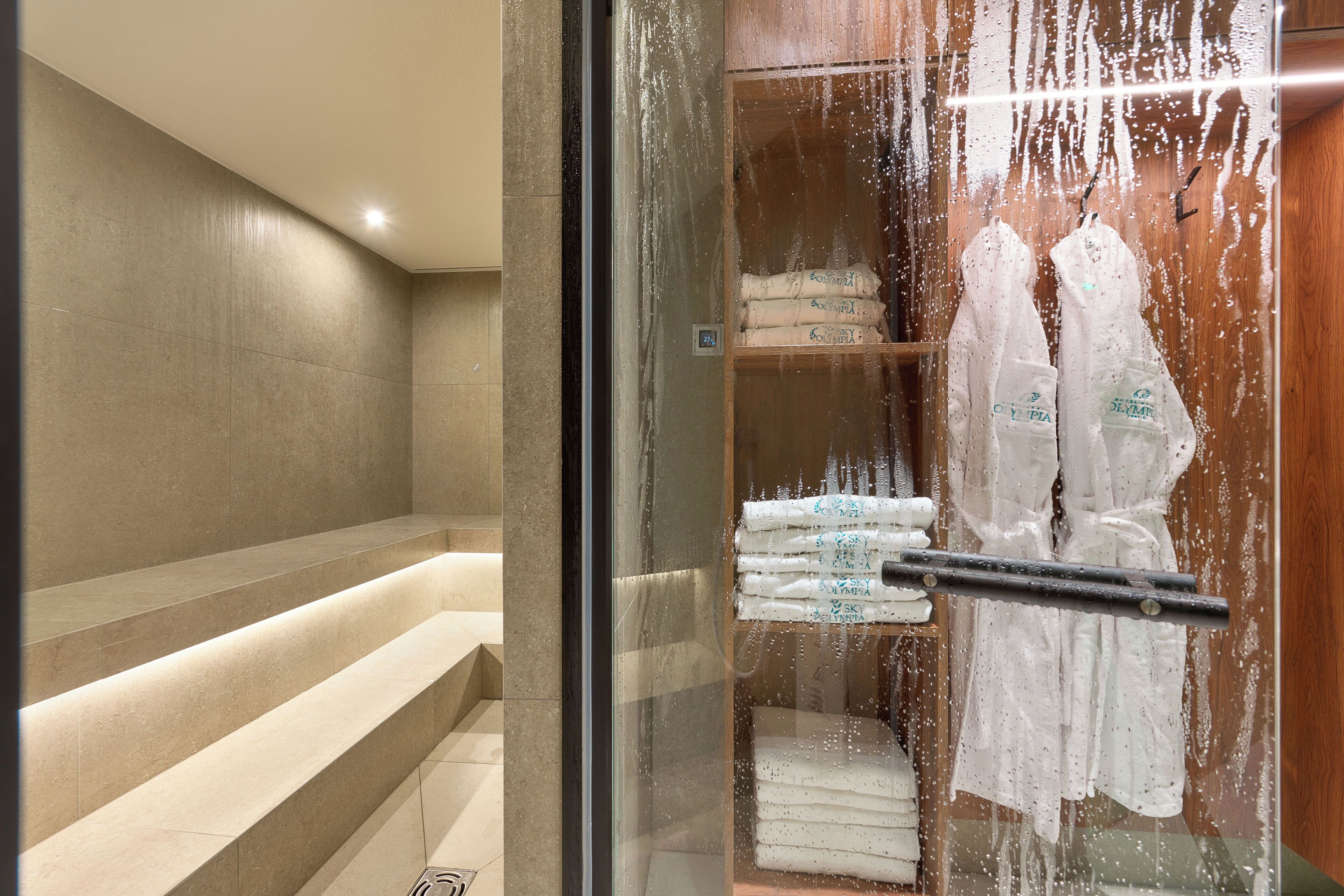 A hotel room with a glass shower enclosure, a wooden vanity, and neatly folded towels on shelves.