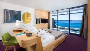 Une chambre d’hôtel moderne dotée d’un grand lit, d’un bureau, d’une chaise, d’une télévision et offrant une vue sur la mer.