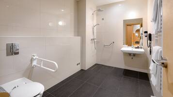 Une salle de bain moderne avec des toilettes blanches, une douche équipée d’un pommeau de douche à main, un lavabo avec un miroir et un porte-serviettes.