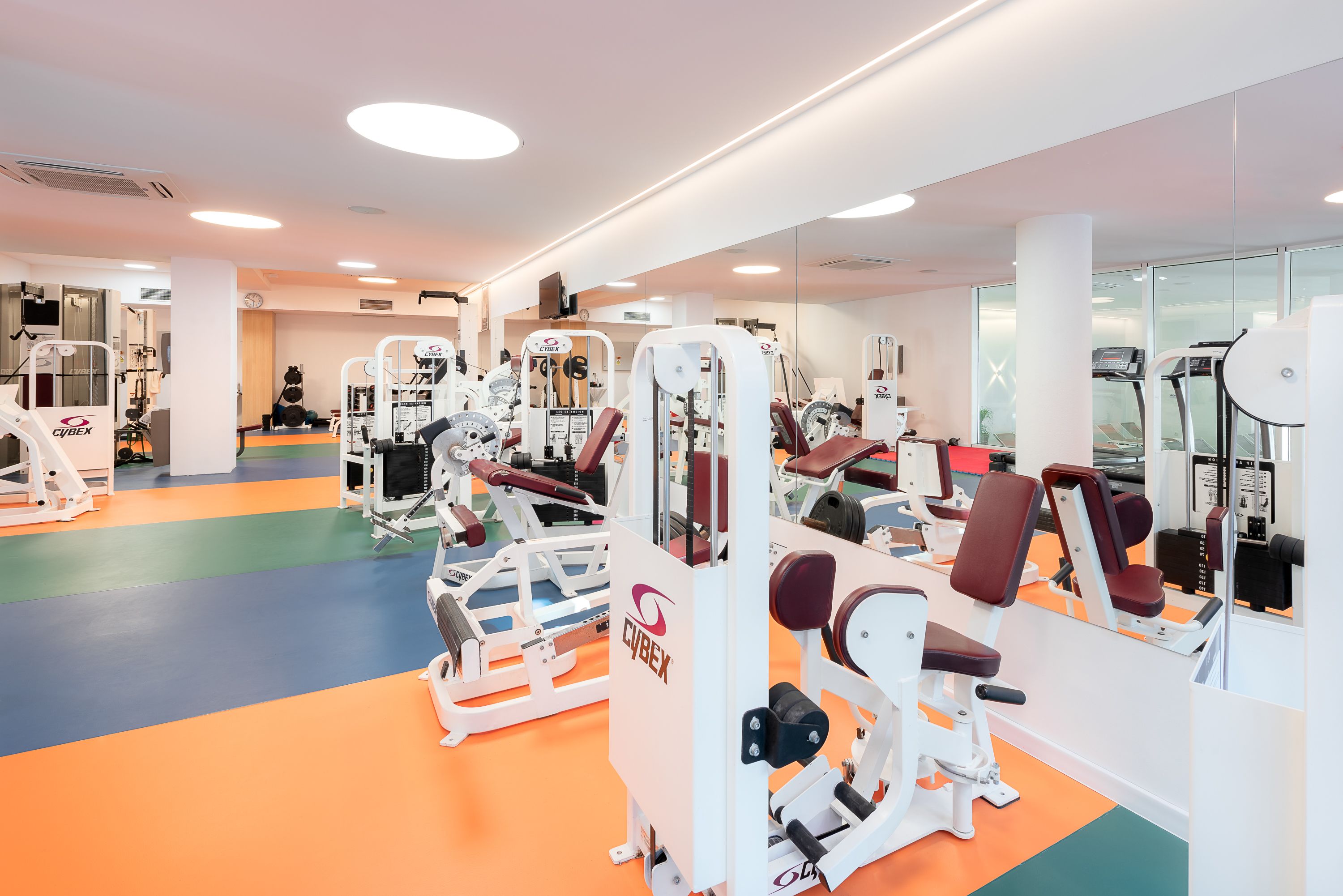 A gym with various exercise machines, a mirror wall, and a colorful floor.
