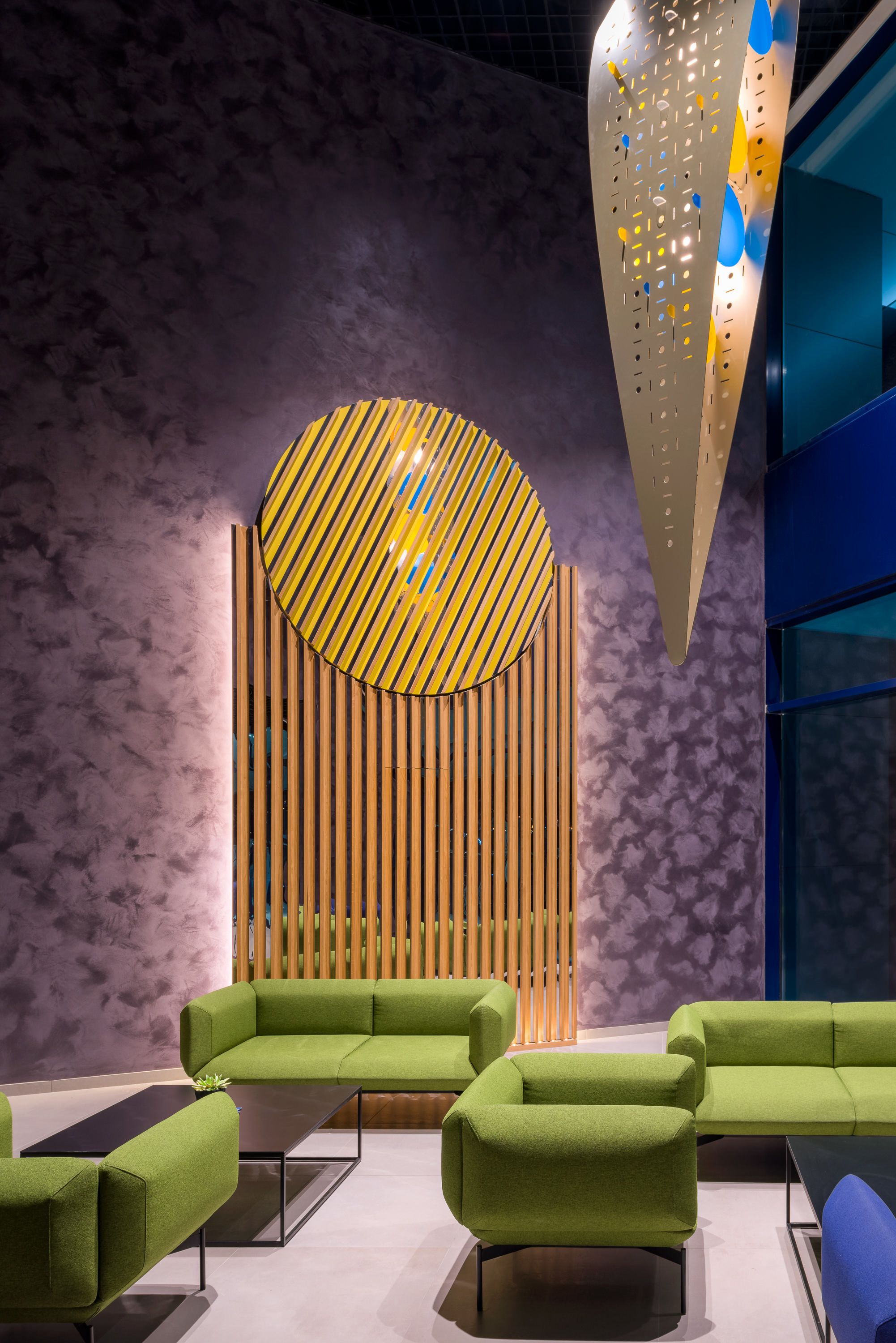 Een moderne lounge met groene banken, een wand van houten latten en een bijzondere plafondlamp.