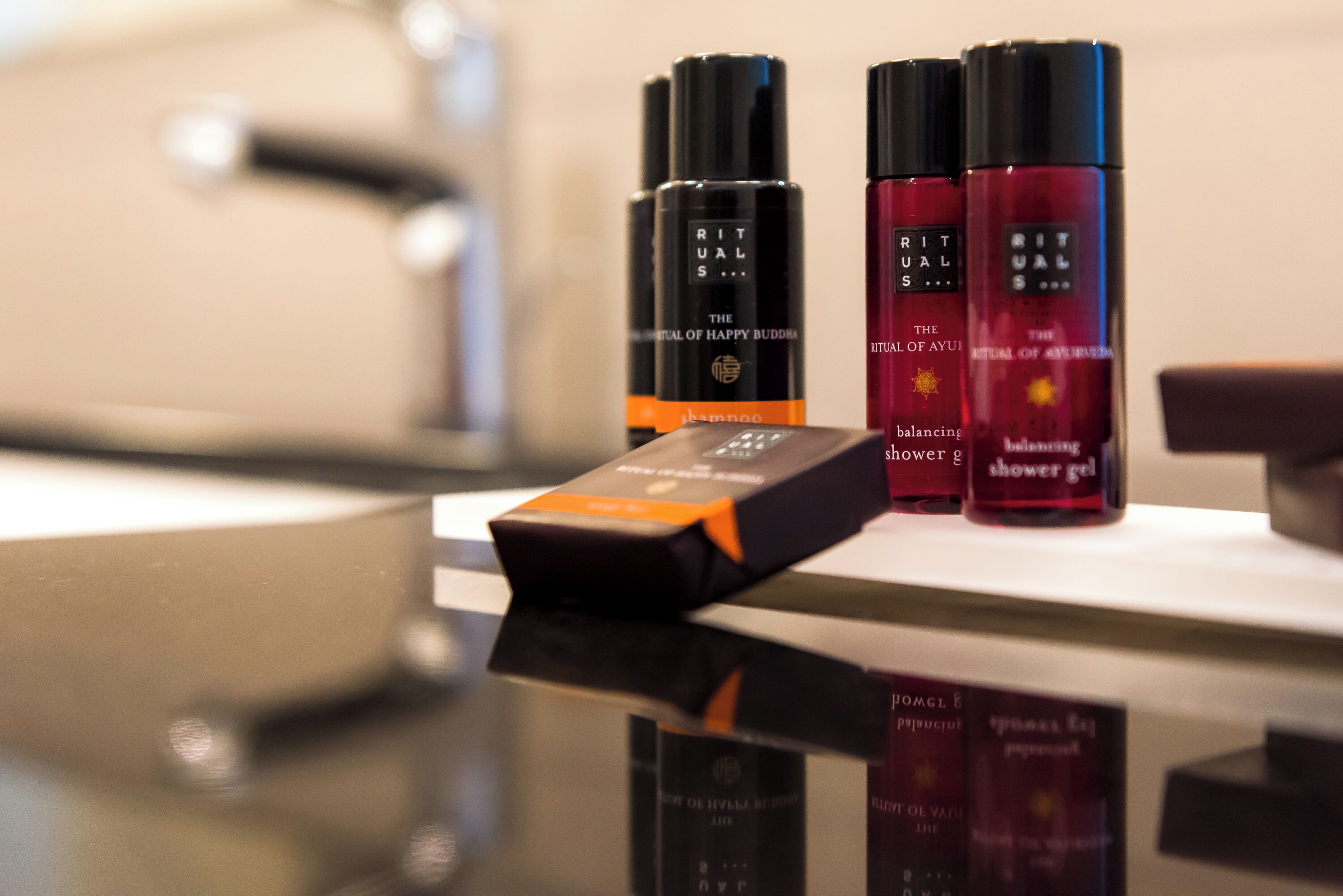 Una encimera de baño con tres botellas de champú Rituals The Ritual of Happy Buddha y dos botellas de gel de ducha Rituals The Ritual of Ayu equilibrante.