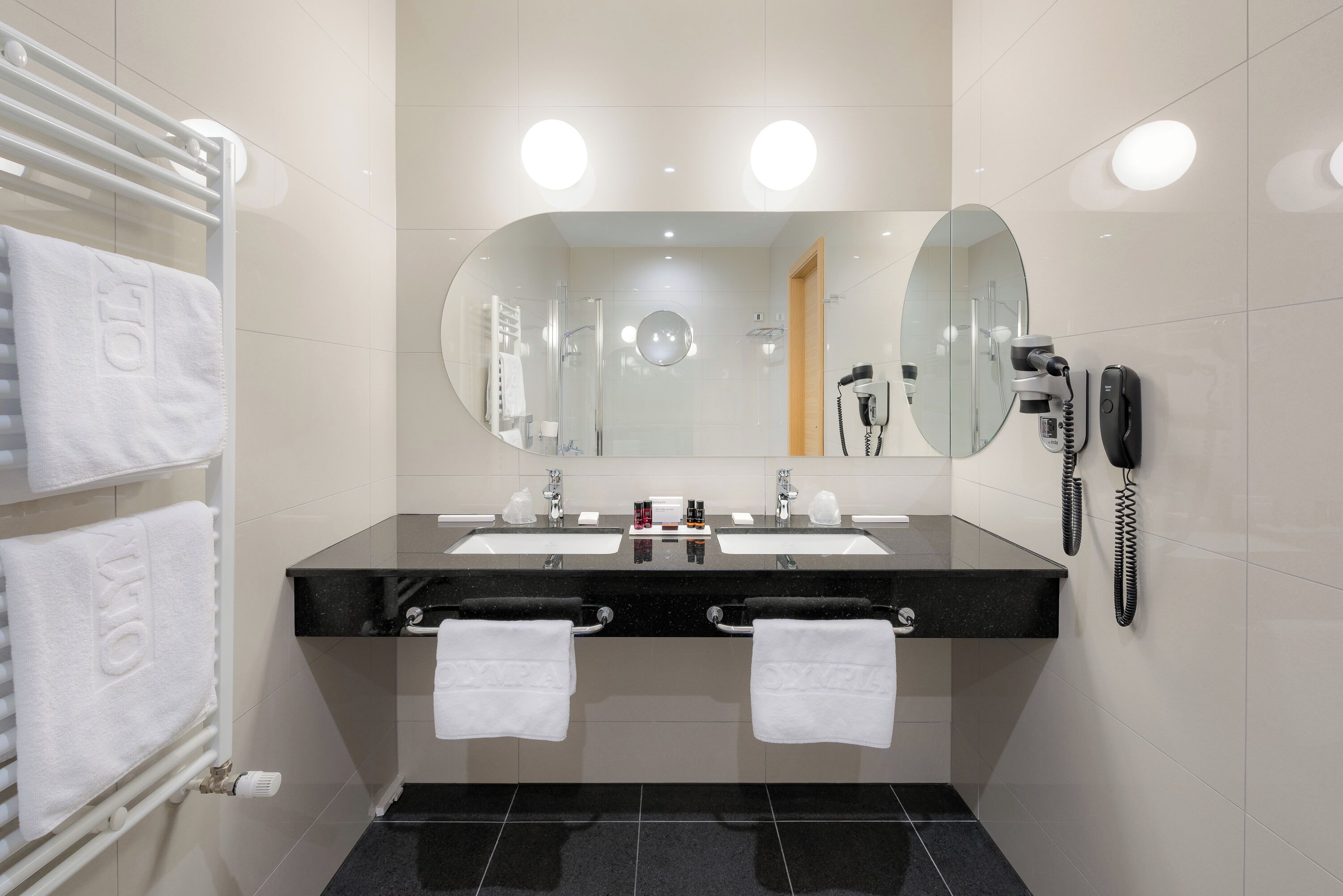 A modern bathroom with a double sink, two towels, a hairdryer, and a telephone.