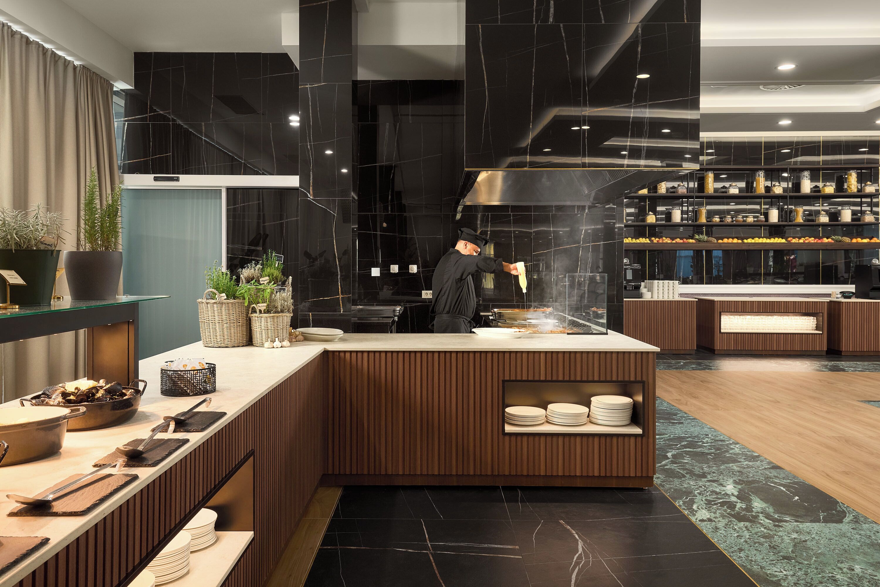A modern kitchen with a chef preparing food, wooden counters, and a marble backsplash.