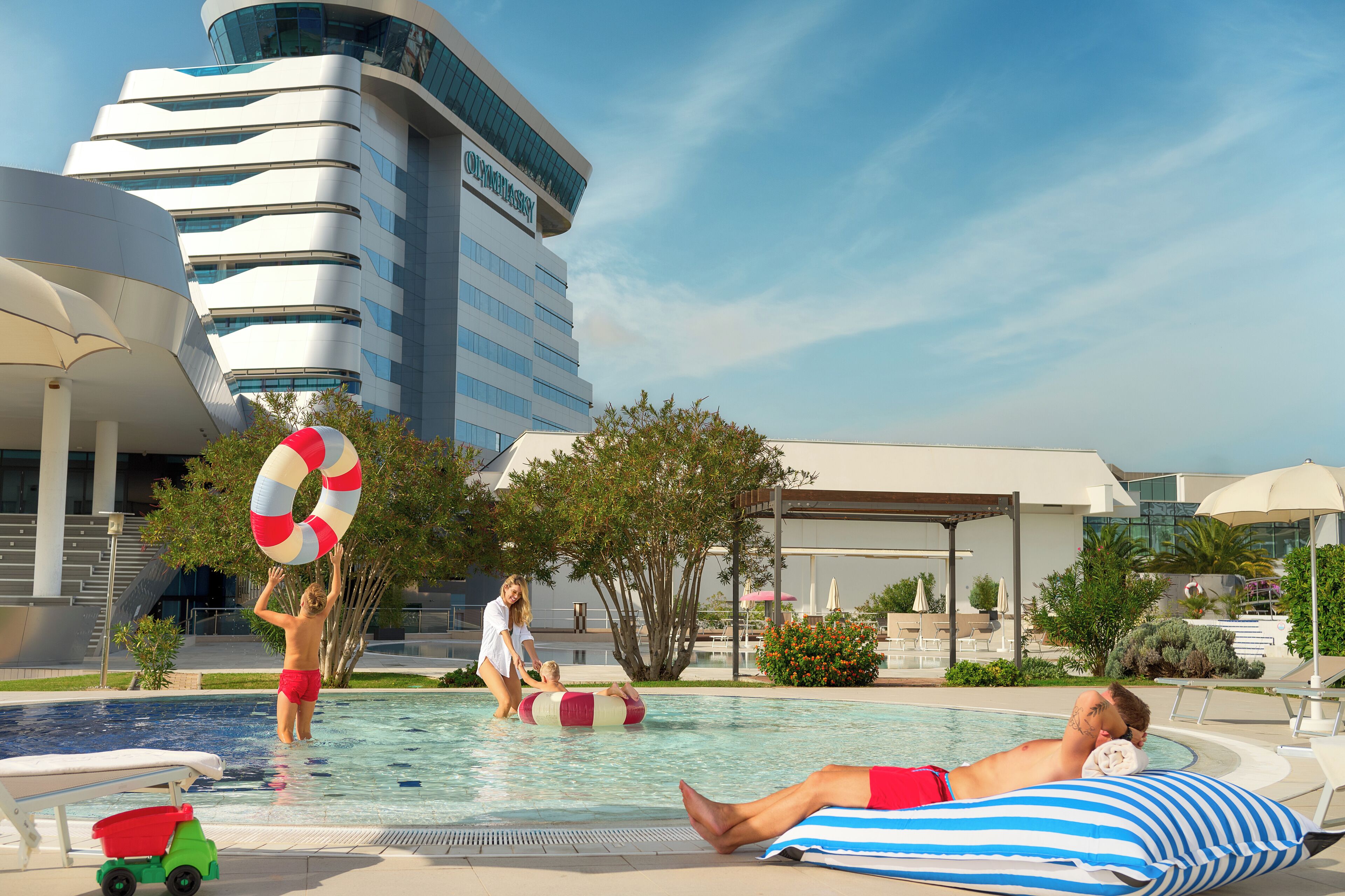 Un espace piscine avec un bâtiment moderne en arrière-plan, des chaises longues et un parasol au bord de la piscine.