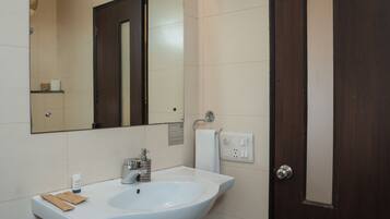 A bathroom with a white sink, a mirror, a wall-mounted fan, and a dark wooden door.
