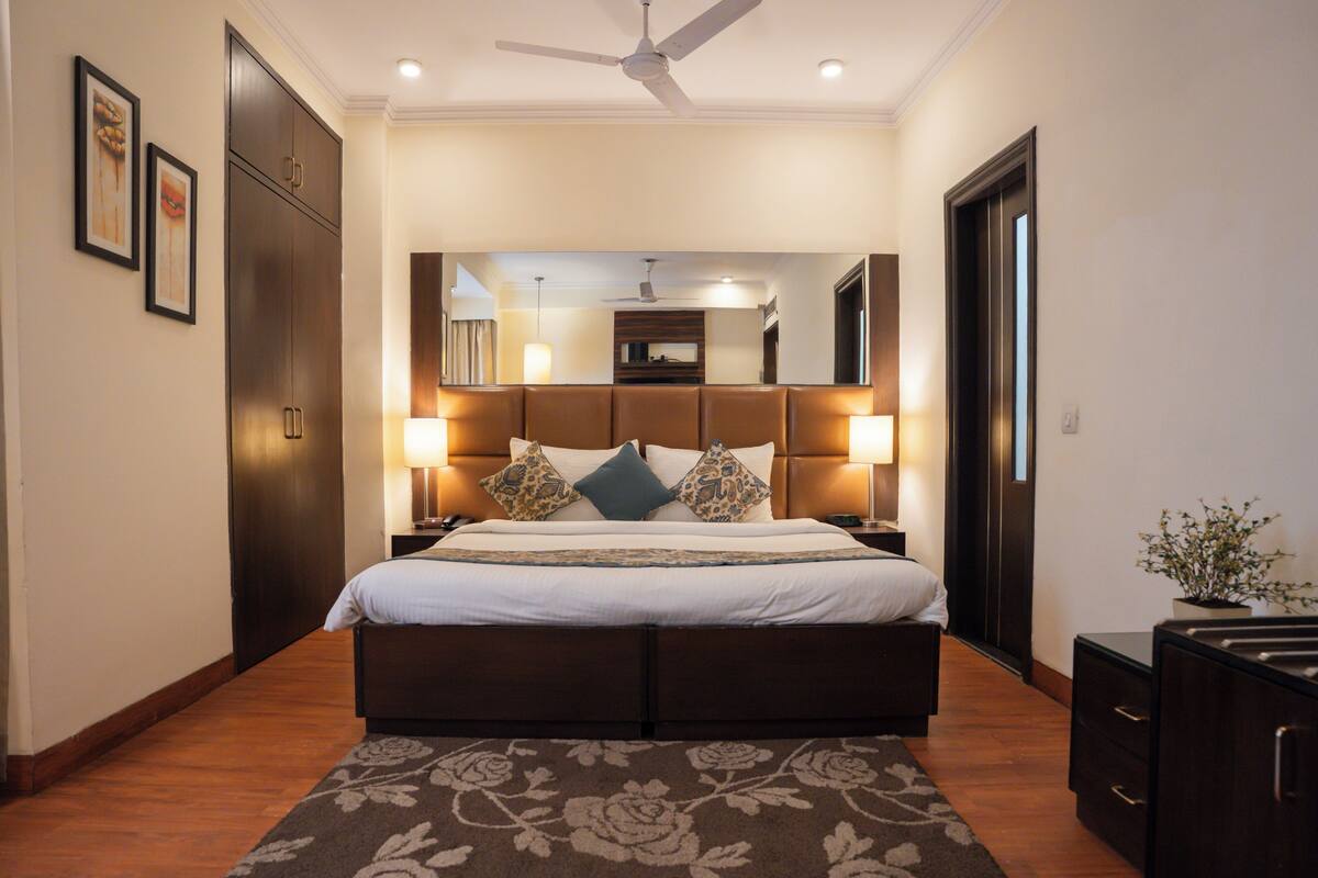 Un dormitorio de hotel con una cama grande, lámparas de noche, un ventilador de techo y suelo de madera.