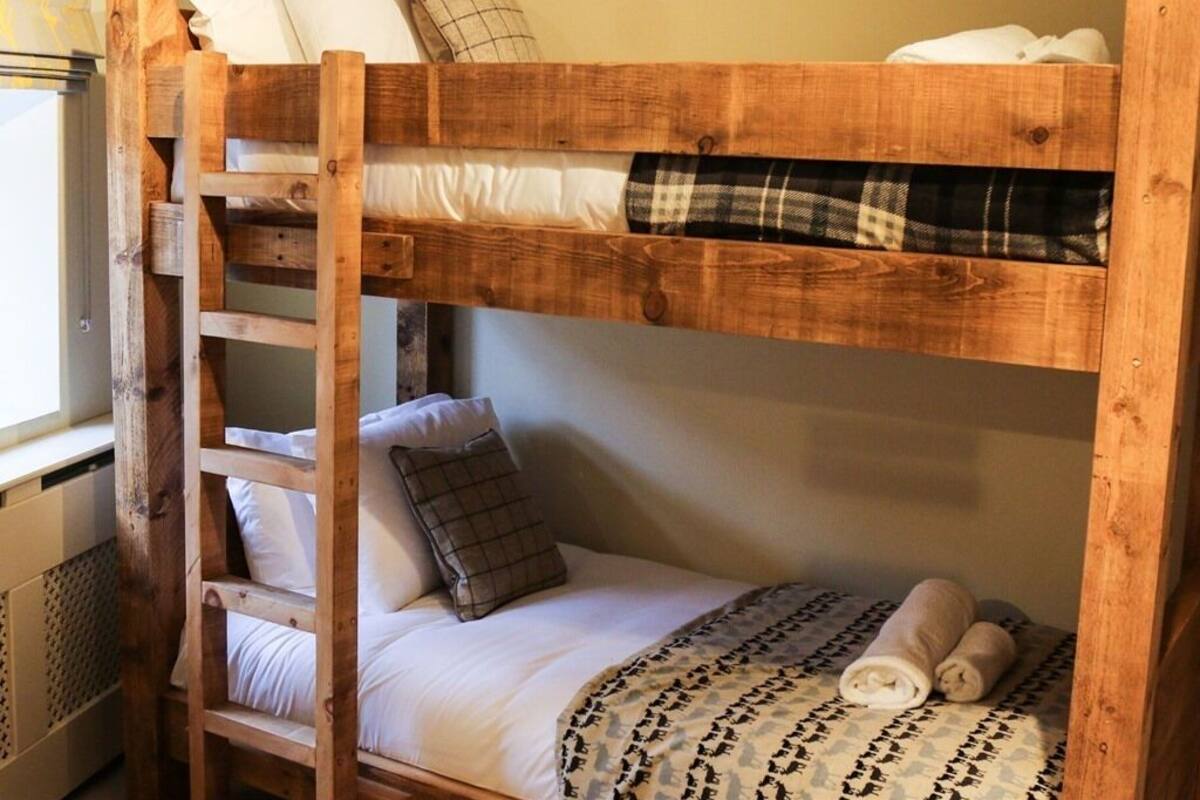 A bunk bed with a ladder, white bedding, and a plaid blanket.