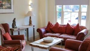 A living room with a red sofa set, a striped armchair, a wooden coffee table, a lamp, and a framed picture on the wall. - The Quay B&B (Wells-next-the-Sea)