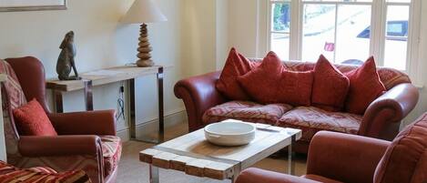 Un salon avec un canapé rouge, un fauteuil à rayures, une table basse en bois, une lampe et un tableau encadré accroché au mur.