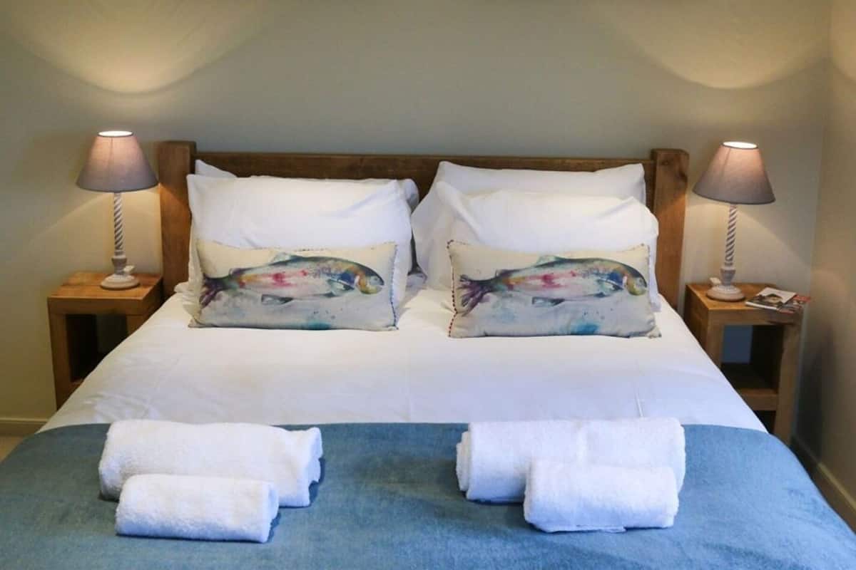 A neatly made bed with white linens and decorative pillows, two bedside lamps, and a blue throw blanket.