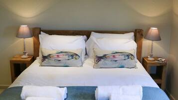 Una cama bien hecha con sábanas blancas, almohadas decorativas, dos lámparas de noche y una manta azul.