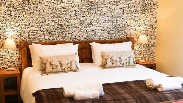 A neatly made bed with two pillows, a red upholstered bench, and a patterned wall. - The Quay B&B (Wells-next-the-Sea)